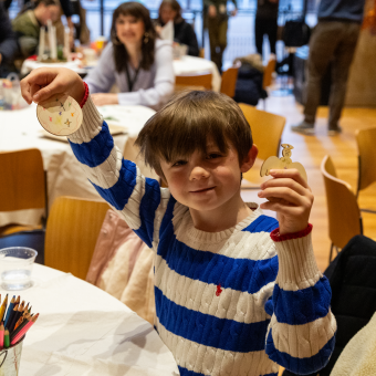 A child smiles and holds up a handmade Christmas tree ornament