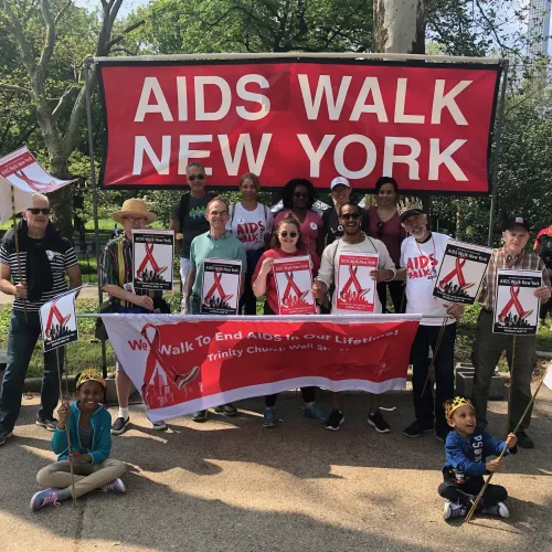 A group of people stand with posters in front of a sign that reads, "AIDS Walk New York."