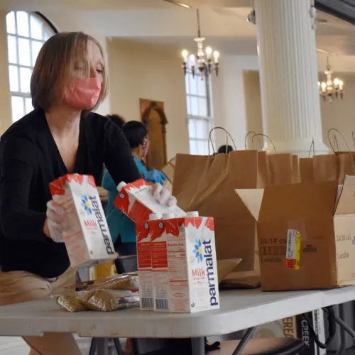 A masked woman packs boxes of milk into brown bags.