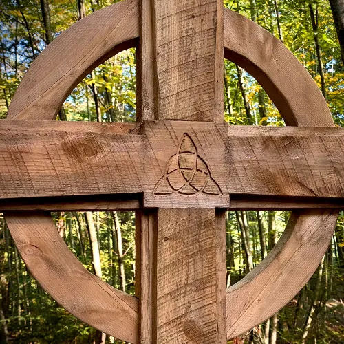 A wooden cross with the green Trinity Forest behind it