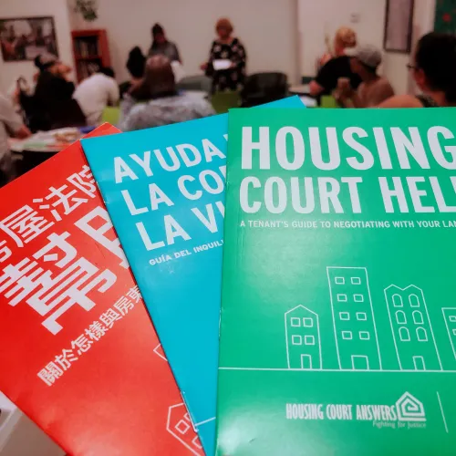 The foreground has three booklets with "Housing Court Help" written in Chinese, Spanish, and English. The background features a small group in conversation.