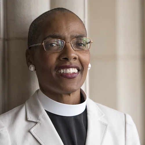 The Very Rev. Dr. Kelly Brown Douglas stands in front of a white wall.