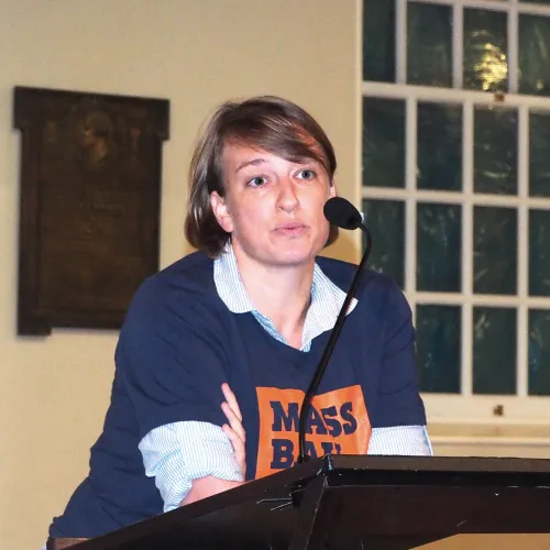 A woman in a shirt that reads "Mass Bail Out" speaks into a microphone.
