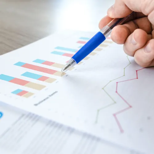 A hand holds a pen, points to a bar graph. A line graph is also on the page.