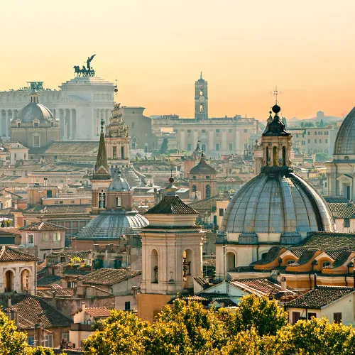 Spires and bell towers make up the skyline of Rome against a sunset