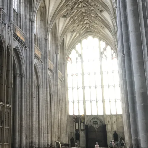 Winchester Cathedral, interior view, grey stone columns, looking towards a large clear stained glass window at the rear of the cathedral.