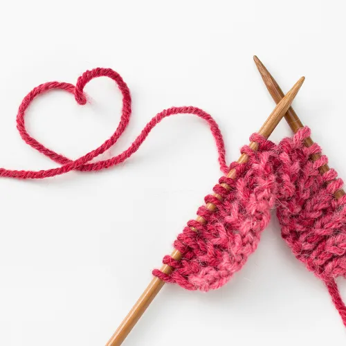 Image of knitting needles with pink yarn in the shape of a heart