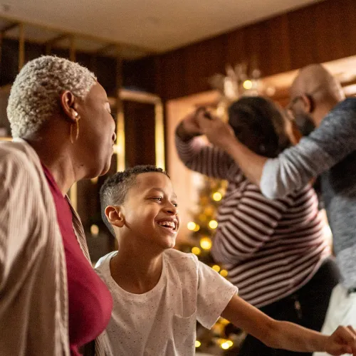 Families dancing in a living room with a Christmas tree