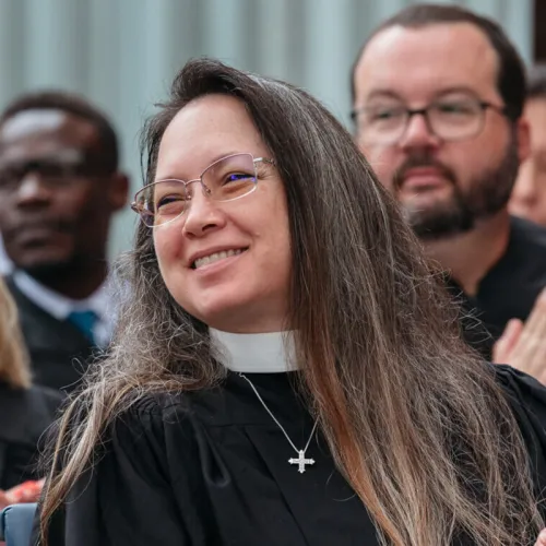 A woman wearing a clerical collar smiles in a crowd