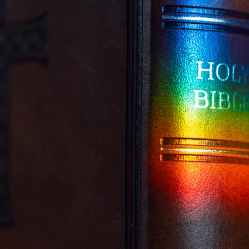 A prism of colored lights shines on the spine of a leather-bound Bible