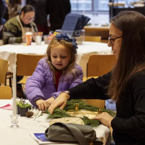 A girl makes a Christmas wreath with a lady.