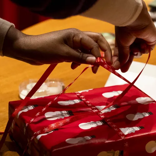 A person wraps a gift with ribbon.